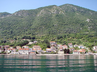 View from the sea to the coastal town of Montenegro at the foot of the hill reflected on the azure sea surface.