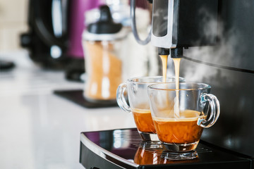 freshly brewed coffee is poured from the coffee machine into glass cups in the kitchen at home