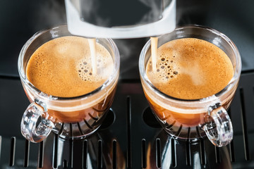 freshly brewed coffee is poured from the coffee machine into glass cups