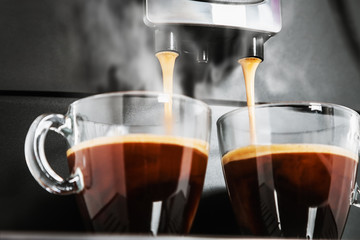 freshly brewed coffee is poured from the coffee machine into glass cups