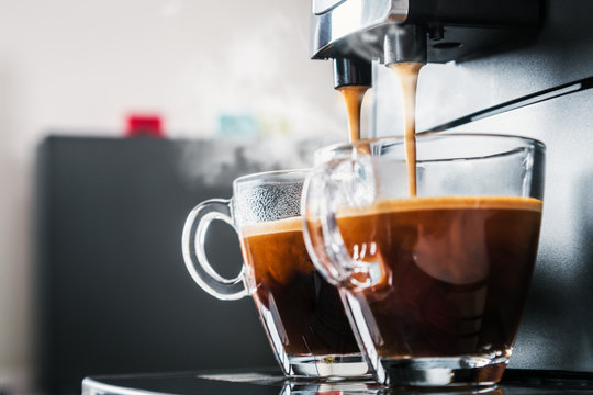 freshly brewed coffee is poured from the coffee machine into glass cups in the kitchen at home