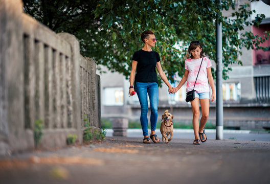 Mother and daughter walking on the street with a dog