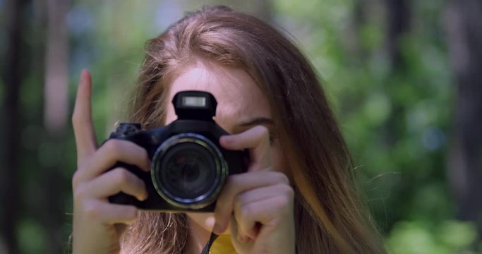 4K Portrait. Girl taking a Photograph with a Camera in Forest. Young Photography Student in a Wood Glade of Trees. Blonde Hair, Pretty Woman in a British Nature Park with Sun Light.