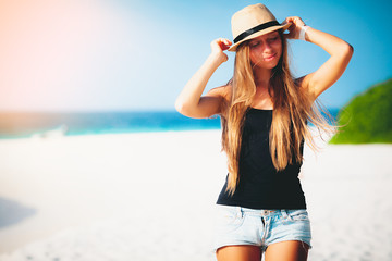 Summer vacation holiday travel tropical beach background - beautiful young Caucasian girl tourist walking on the lagoon at sunset with hat near the sea on the exotic island smiling enjoying