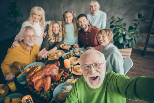 Photo of big family sit hugging feast dishes table around roasted turkey multi-generation relatives grey-haired grandpa making group selfies in living room indoors