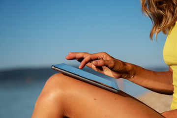 Woman sitting on the beach browsing on her digital tablet