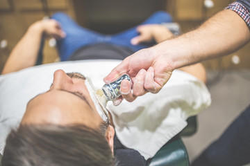 Professional hairdresser applying shaving foam on client skin in barbershop.