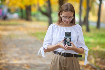 Attractive beautiful young girl holding retro vintage twin lens reflection camera in autumn park.