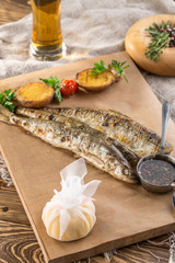 Fried smelt fish, lemon slice and potato wedges on paper and glass of beer on wooden table
