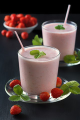 Strawberry smoothie or milkshake in glass cup on black rustic background, healthy food for breakfast and snack