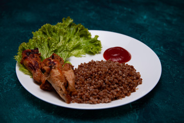 fried chicken thighs with lettuce, buckwheat porridge and sauce on a white plate