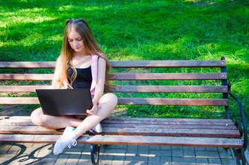 girl with a laptop on a bench in the park on a background of greenery