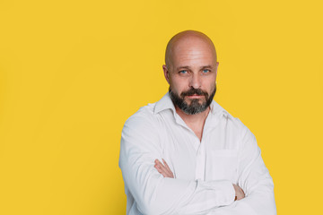 Obraz premium Serious middle-aged man with folded arms and a deadpan expression posing in front of a yellow background with copy space