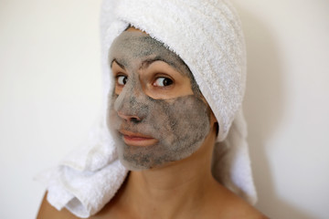 Young woman with a black bubble charcoal oxygen mask on her face and towel on the head. Beauty spa acne treatment. Popular face mask.