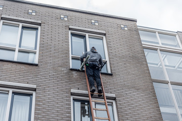 Window cleaner on a ladder cleaning the windos high against a building of brick walls.
