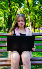 girl with a laptop on a bench in the park on a background of greenery