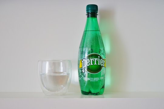 NEW YORK CITY, NY -4 OCT 2019- View of a glass and green plastic bottle of carbonated mineral water from Perrier, a French sparkling water brand.