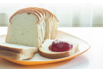 Loaf of bread sliced in a plate with mixed fruit jam on a table near window with sunlight