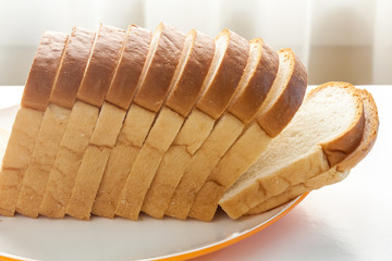 Loaf of bread sliced in a plate on a table near window with sunlight