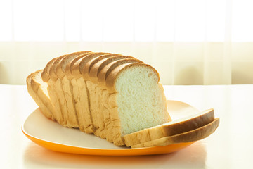 Loaf of bread sliced in a plate on a table near window with sunlight