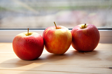 three apples on a wooden background near the window