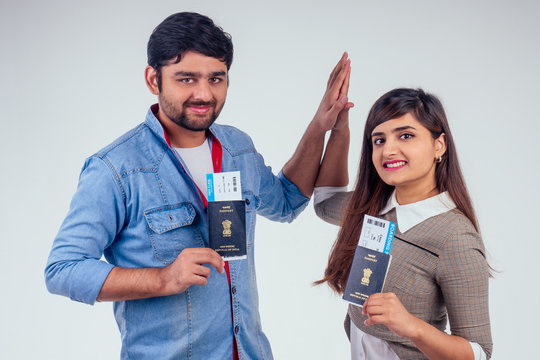 happy indian couple holding passport of India with airline tickets inside in studio white background and giving high five