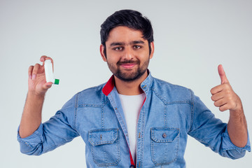 Young indian man in a denim jeans jacket using asthma inhaler at studio white background