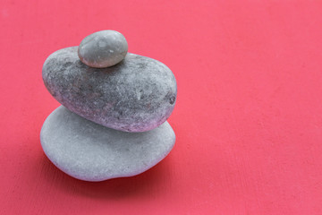 Two large and one small smooth polished stones by the sea lie on each other on a coral background, side view from above
