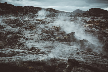 Leirhnjukur old black lava field with stones and smoke coming from ground in Iceland, overcast day in summer , film effect with grain