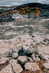 Leirhnjukur old black lava field with colorful stones and smoke coming from ground and blue sky in Iceland, overcast day in summer , film effect with grain
