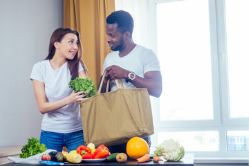 multinational couple unloading a bag from products choosing textile or polyester bag.african american man and asian woman coming home after the store