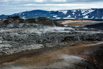 Leirhnjukur old black lava field with colorful stones and smoke coming from ground and blue sky in Iceland, overcast day in summer , film effect with grain