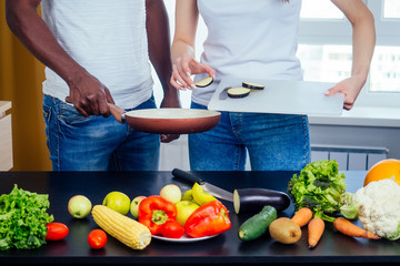 Korean woman wearimg white cotton t-shirt with her african american boyfriend cooking in fry pan bresksast