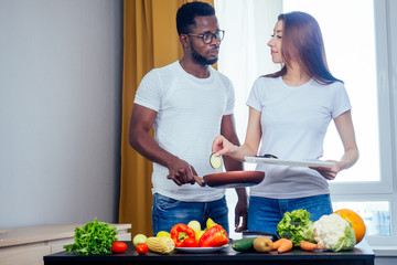 Korean woman wearimg white cotton t-shirt with her african american boyfriend cooking in fry pan bresksast