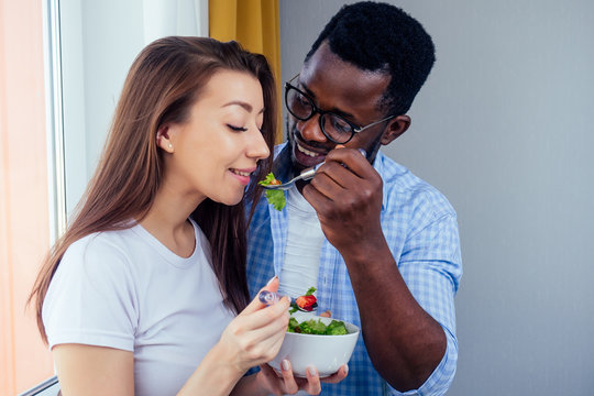 african american man eating salad with woman in living room