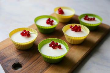 Italian dessert panna cotta with fresh red currants served in silicon molds form on wooden tray and white background.