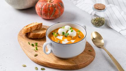 Vegetarian autumn pumpkin cream soup with seeds and mozzarella balls on white background with pumpkins and bread. Menu, restaurant. Vegeterian seasonal food.