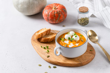Pumpkin cream soup with coconut milk, pumpkin seeds and mozzarella balls on a white concrete...