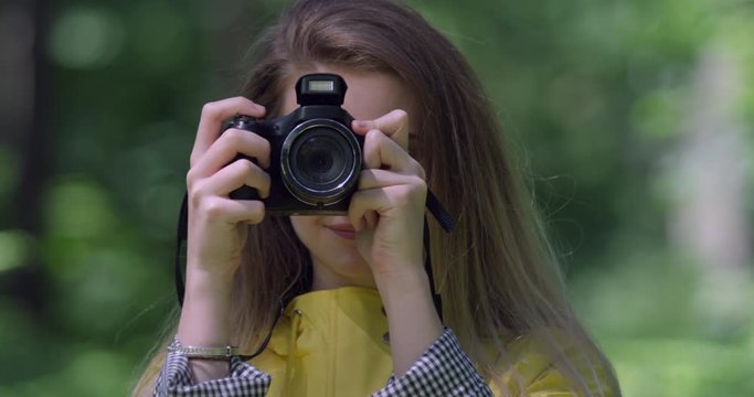  Young Girl with Camera in a Forest. Young Student taking photographs in Yellow Rain coat  within the Woods. Gap Year Traveller with Blonde Hair, Pretty Woman in a British National Trust Park 