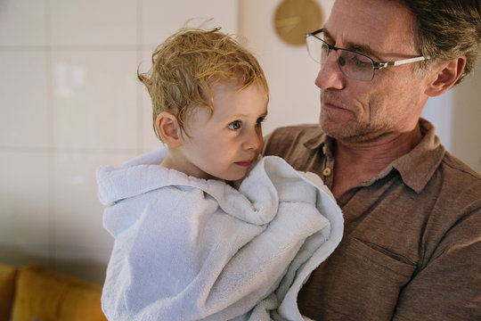 Father carrying bathed toddler in white towel
