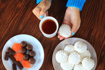 woman's hands with a mug of tea and marshmallows, a plate of marshmallows, a plate of sweets and marmalade