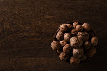  Walnuts nuts in a bowl on a dark brown wooden background in a dark key