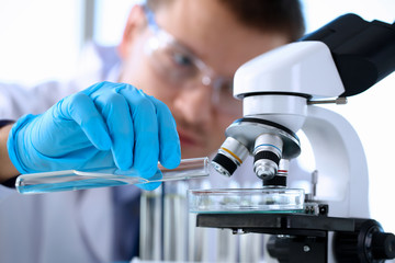 Male chemist holds test tube of glass in hand portrait overflows liquid solution potassium permanganate conducts an analysis reaction takes various versions of reagents using chemical manufacturing.