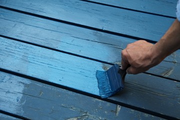 Hand is painting a wooden terrace with blue wood preservative paint, exterior