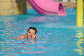 Active Caucasian boy spending his summer holidays in water park, he splashing in pool against...
