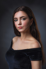 Naklejka premium Portrait of a young beautiful girl in a black dress, close-up. Model with dark hair posing near the wall