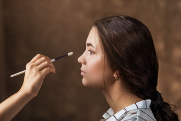 Makeup artist applies nude makeup to emphasize the natural beauty of the girls face. Profile view