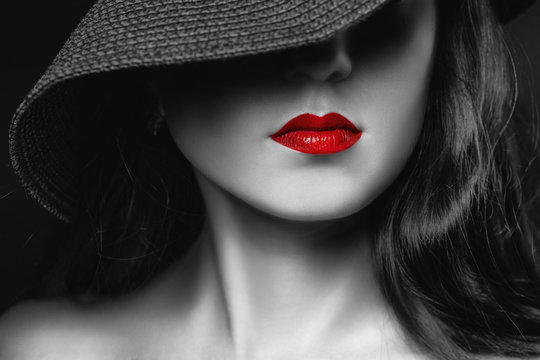 Beautifully painted red lips on the girl's face. Model in a black hat close-up