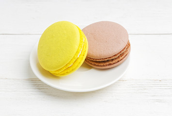 Close-up two macaroons lemon and chocolate on white plate on white wooden table
