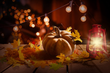 Halloween or Thanksgiving background with fresh fall pumpkins on straw lit by a burning lantern and sparkling part lights behind with copy space